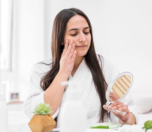 Woman in a white robe looking into a mirror and touching her face while checking her dry skin condition.